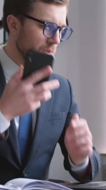 Amerikan görünümlü genç bir yatırım bankacısı bilgisayar üzerinde çalışırken telefonla konuşuyor. Meşgul müdür. Ofiste çalış.