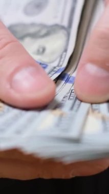 Erkek eli, 100 dolarlık banknotları sayıyor. Yatırım, rüşvet veya yolsuzluk konsepti. Seçici odaklanma. Dikey video
