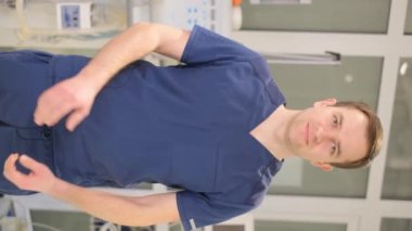 Vertical portrait of a young doctor looking at the camera while standing in a modern clinic. Free medicine in Europe