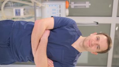 Portrait of a young male doctor in blue medical special clothes. An employee of a medical clinic. Vertical video