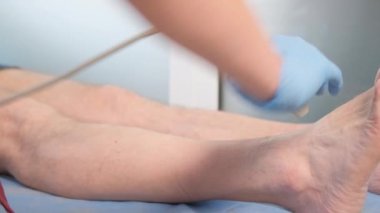 A female doctor uses sonography to take an x-ray of a patients knee. Treatment of the legs of an elderly patient