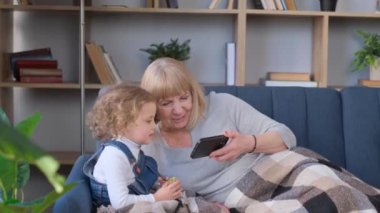 Grandmother and granddaughter use a smartphone, they have fun together.