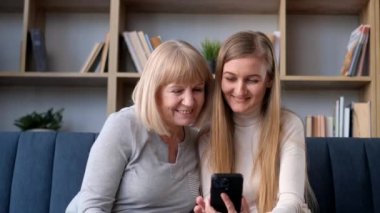An elderly woman and her daughter hug while sitting on the sofa. Happy grandmother and daughter.