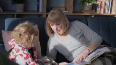 Happy grandmother spends time with her granddaughter at home. Relaxing on the couch.