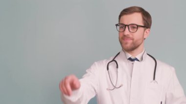 Amerikan görünümlü genç bir doktor beyaz bir sağlık üniforması içinde ve birini işaret ediyor. Arka planda bir terapist. Arka planda genç bir doktorun fotoğrafı..
