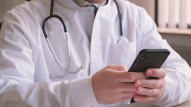 Ofisteki masada oturan genç profesyonel doktor akıllı telefona bakıyor. Doktorlar gündüzleri çalışıyor. Terapist özel muayenehanesi