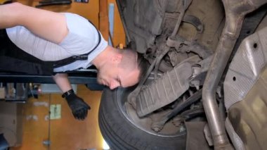 Araba şasisini tamir eden bir araba tamircisinin dikey videosu. Araba tamiri kavramı. Dikey video.
