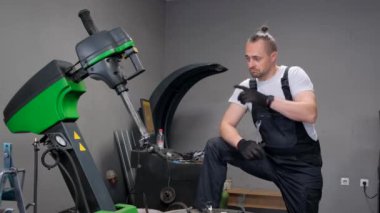 Portrait of a car mechanic pointing his finger away, balancing wheels, changing tires seasonally, solving rims, problems with replacing broken parts.