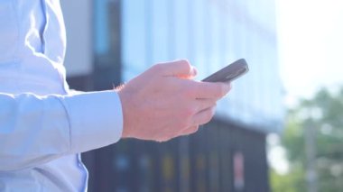 Bir iş merkezinin arka planında akıllı telefon kullanan genç bir iş adamının yakın çekimi. Dikey video
