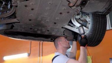 A car mechanic fixing a car from below. The craftsman repairs the chassis of the car. The concept of car repair