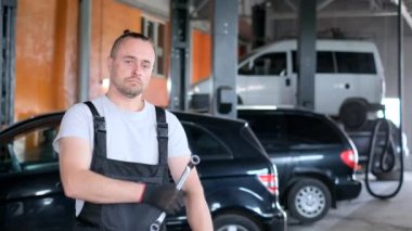 Portrait of handsome american auto mechanic holding wrenches and looking at camera. Professional mechanic