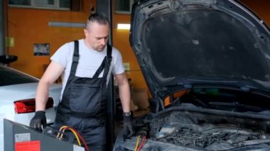 A car mechanic fills up the air conditioner. Maintenance and regulation of freon supply to the system. Car service processes.