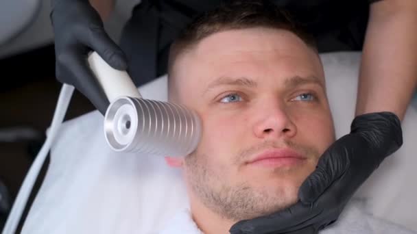 用现代电按摩器对一个年轻貌美的男人进行面部按摩 男性年轻化美容术 — 图库视频影像