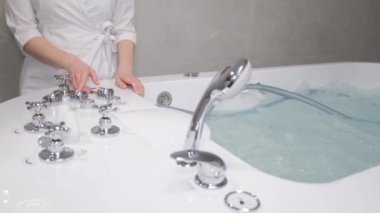 A young spa cosmetologist girl adjusts the hydrobath before the procedure. Hydromassage bath in the salon. Correct water temperature.
