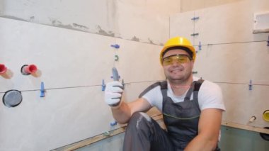 Construction worker sitting on floor and showing thumb up and smiling looking at camera. Home renovation concept
