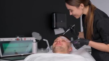 Eldiven takan bir dermatolog bir adamın yüzüne maske takar. Dermatoloji kliniğinde bir adamın yüzüne cilt bakımı. Terapötik yüz maskesi