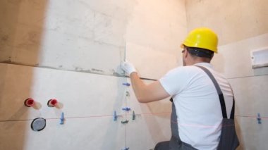 Döşeme ustası banyonun duvarına fayans döşeme işini yapıyor. Döşeme işe yarıyor. Dikey video.