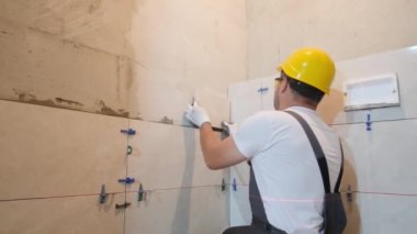 Döşeme işe yarıyor. Tiler, banyo duvarına fayans döşeme işini yürütür. Tiler, duvara büyük ölçekli fayanslar yerleştirir. Dikey video