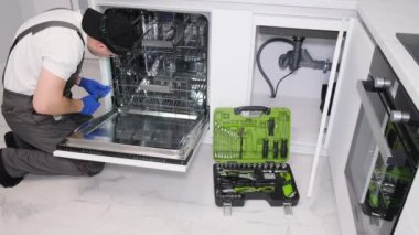 A professional repairman repairs a broken dishwasher in a modern kitchen. Mechanical breakdown of the dishwasher