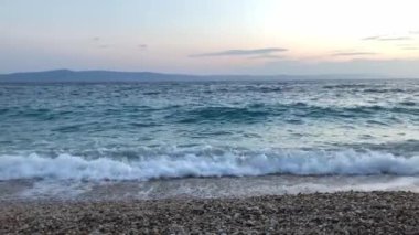 Waves in the sea at sunset. Pebble beach at sunset. Empty shoreline pebble beach. Scenic ocean coastline.