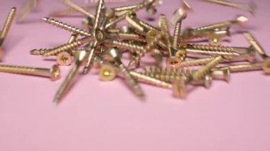 Many metal bolts on a pink background. Super slow motion.