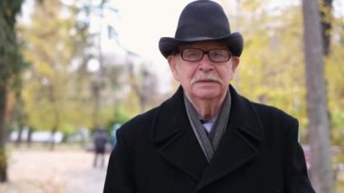 A kind old grandfather in a hat walks in the autumn park and looks at the camera. Healthy elderly people. Autumn colors