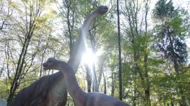 En büyük dinozorlar. Yavrularıyla birlikte bir anne dinozor ormanın ortasında duruyor. Uzun boyunlu bir dinozor. Otçul dinozorlar. Paleontoloji.