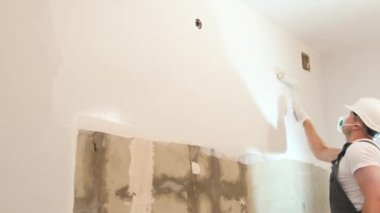 A man paints a wall white. The man is making repairs in the room. Modern interior in the house. Home renovation concept
