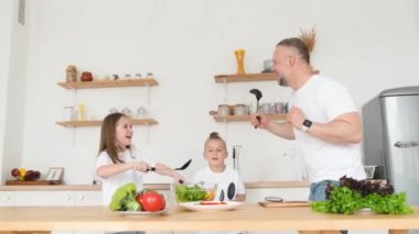 Babam mutfakta evde yemek pişirirken çocuklarla dans ediyor. Mutlu bir aile. Vejetaryen sağlıklı yiyecekler.