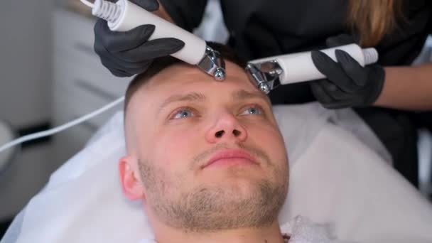 一个年轻英俊男子的面部滚筒按摩 一位美容师用现代工具为男性面部按摩 使其恢复青春 — 图库视频影像
