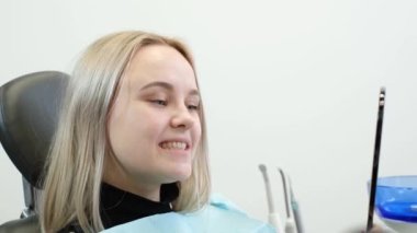 Tatmin olmuş bir hasta iyileşmiş dişlerdeki diş aynasına bakar. Kadın, doktor ve diş muayenehanesi. Diş hastalıklarının zamanında ortadan kaldırılması.