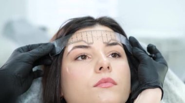 A cosmetologist performs a permanent eyebrow make-up procedure using a special tattoo needle. A woman in a beauty salon. Eyebrow tattoo. The pigment is injected under the skin. Cosmetology