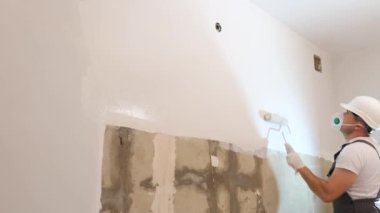 The builder paints the wall white. The man is making repairs in the room. Modern interior in the house. Apartment renovation concept