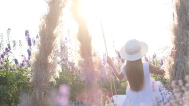 Beyazlar içinde genç bir bayan bir tarlanın ortasında salıncakta sallanıyor. Güzelliğin tadını çıkar. Lavanta renkli fotoğraf oturumu.