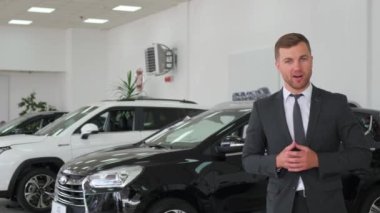 Portrait of handsome European car salesman posing at workplace in car dealership, dealership manager talking about new car.