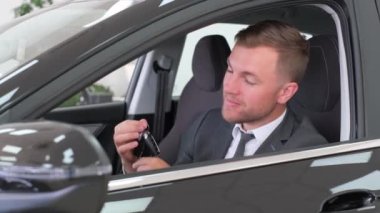 Young european driver in car, sharing concept, vehicle and premium transport. Happy guy driving, sitting in a new luxury car, showing the keys