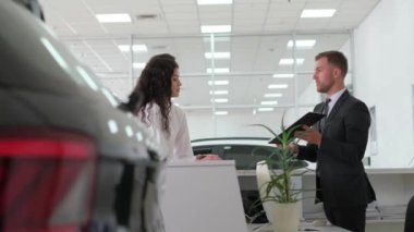 A young couple signs an order for the purchase of a car at the companys office. A car dealer works with a European couple at a car dealership and talks about buying a new car. Salesman.
