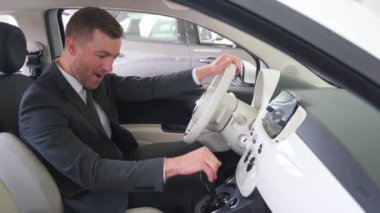 Young man driving a new luxury electric car in a car showroom. The buyer chooses a car.