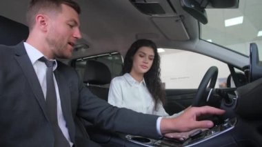 A beautiful brunette girl chooses a new car at a car dealership. A woman examines the interior of a car. The girl is delighted with the new car. 