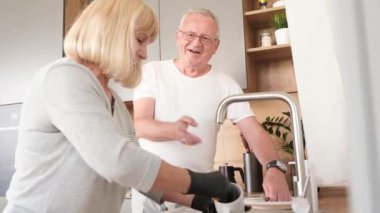 Happy Australian retirees wash dirty dishes after breakfast. An elderly couple spends time in the kitchen