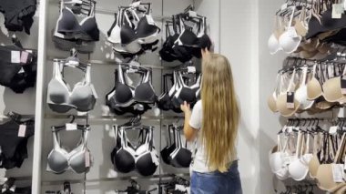 A young woman examines the fabric of the bra she is holding in her hands, looks at the size and price. Underwear store for women