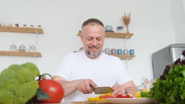 キッチンの自宅で赤と黄色の唐辛子をカットする男 ベジタリアン料理 バーティカルビデオ — ストック動画