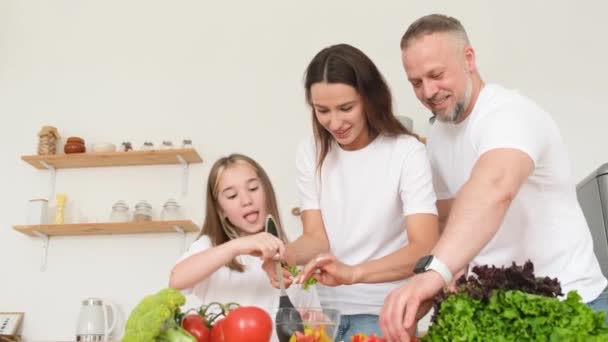 家庭のキッチンで健康的な食べ物を準備している子供たちと一緒に幸せなカップル 野菜サラダの準備 ベジタリアンフード — ストック動画