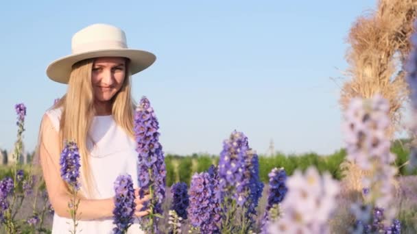 一位戴着白帽的年轻女子 坐在蓝天下的薰衣草花丛中 欣赏着美丽的景色 美丽与享受大自然的概念 — 图库视频影像