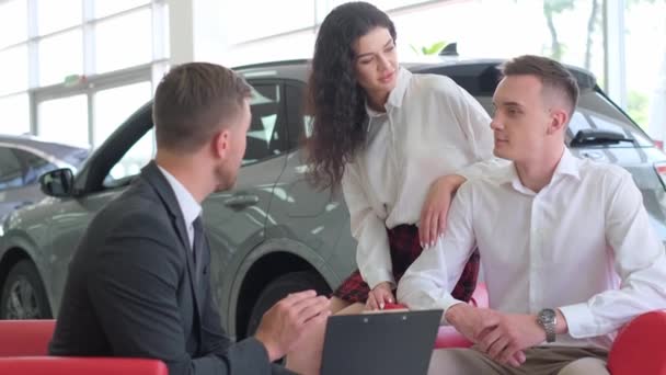 Young Couple Talking Sales Consultant Car Shop Telling Them Car — Vídeo de stock