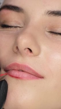 Kalıcı dudak makyajı sırasında genç ve güzel bir esmer. Güzellik salonunda. Modern kozmetoloji. Dikey video