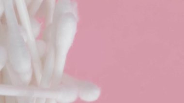 Pembe arka planda pamuklu çubuklar, plastik pamuklu bezler. Dikey video.