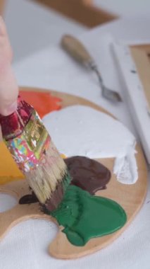 The hand of a young artist mixes paints on a palette that stands on the table. Basic colors. Work with a thick paintbrush. Workplace of the artist