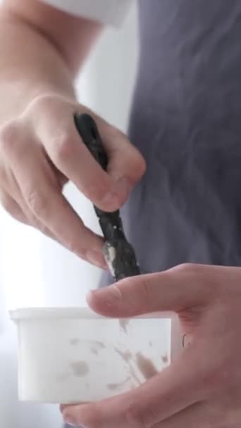这位艺术家站在那里 用铲子搅拌容器中的白漆 白色调的创意工作坊 创建一个画面的过程 刷毛运动 垂直录像 — 图库视频影像