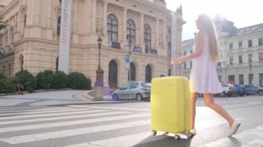 Genç bir bayan gezgin, elinde bavulla şehir caddesinde yürüyor. Yolculuk sırasında şehre varmak. Güzel turist kız seyahat eder.